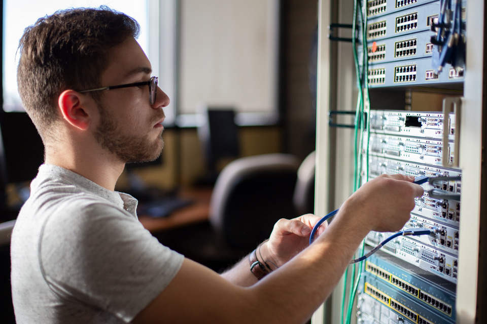 Male student plugging cables into a server