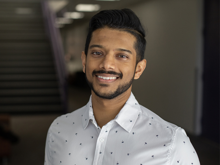 Diverse male student smiling into the camera against muted background wall